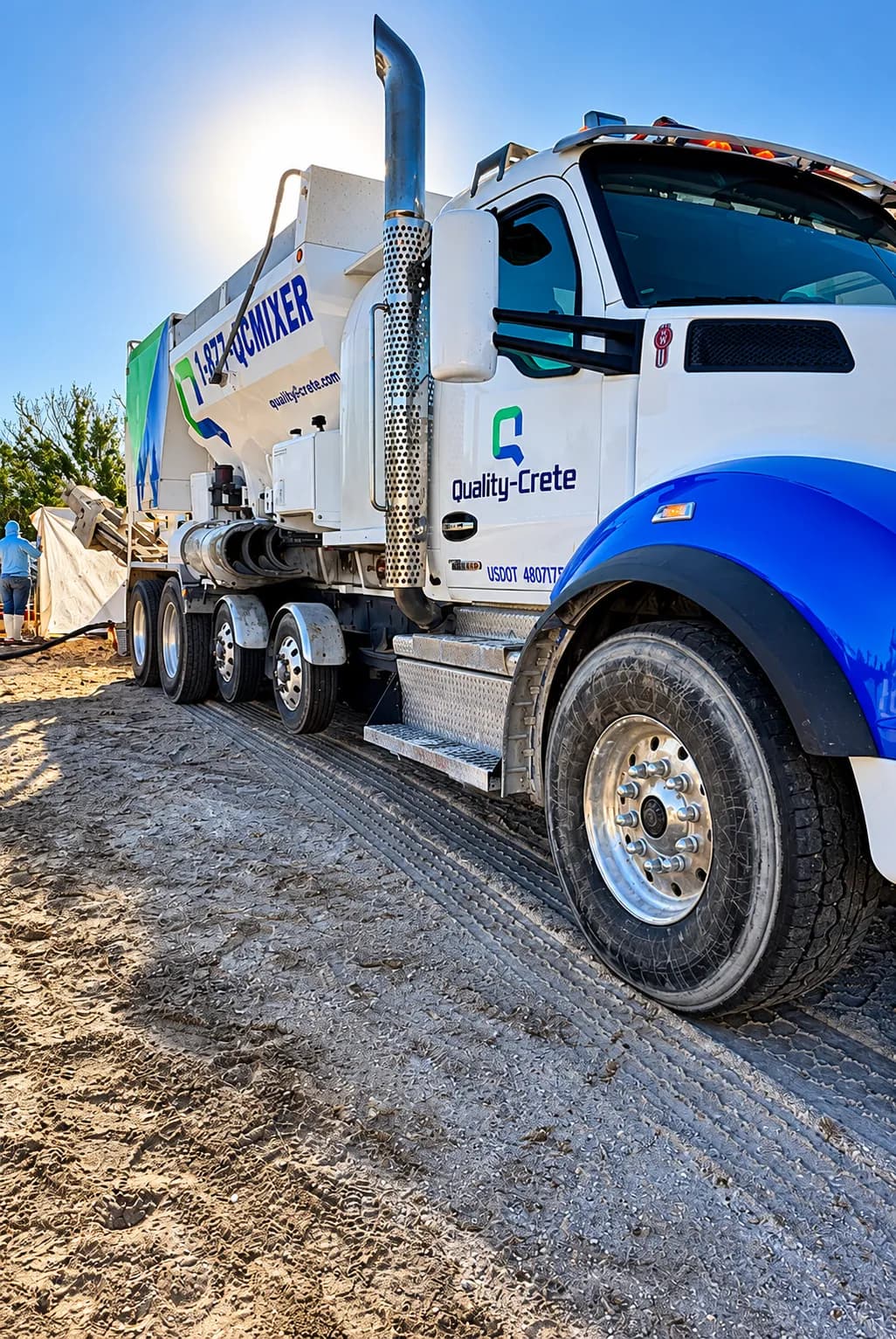 White and blue Quality-Crete volumetric mixer truck on a jobsite
