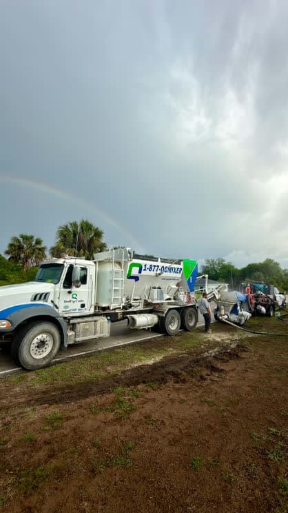 Quality-Crete volumetric mixer discharging concrete on a jobsite under a rainbow