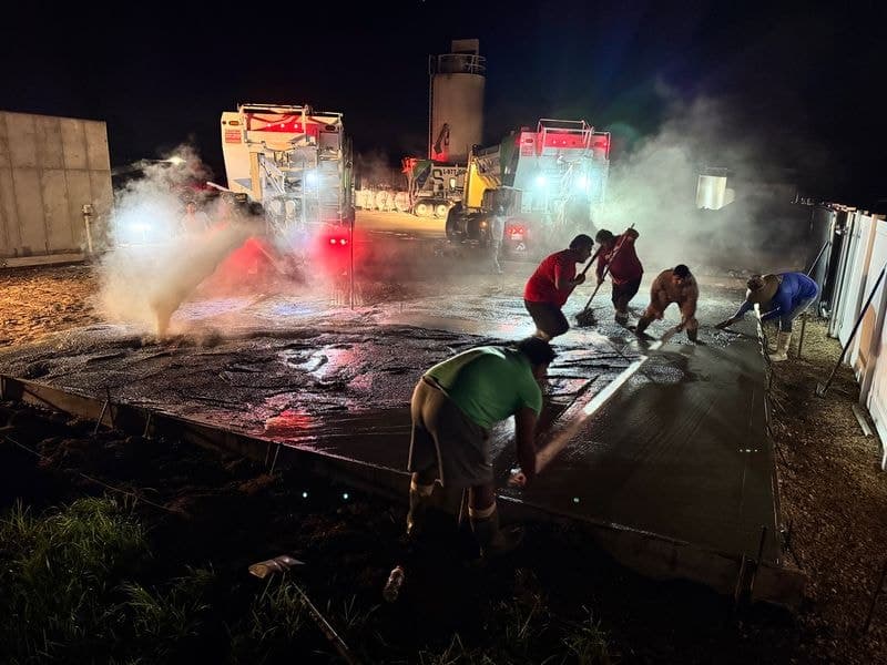 Crew finishing a freshly poured slab at night beside two Quality-Crete volumetric mixers under work lights