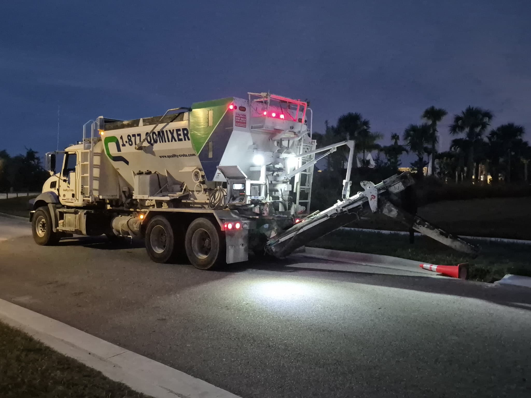 Quality-Crete volumetric mixer truck parked on a roadside at night, lit by its own work lights