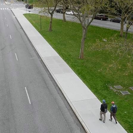 Wide concrete sidewalk along a tree-lined street with pedestrians walking