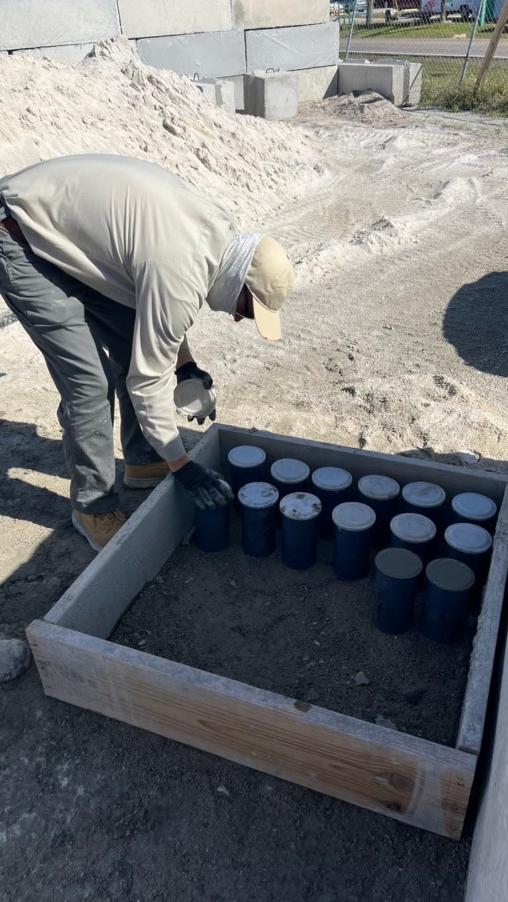 Quality-Crete crew member arranging concrete test cylinders in a field mold box at a jobsite