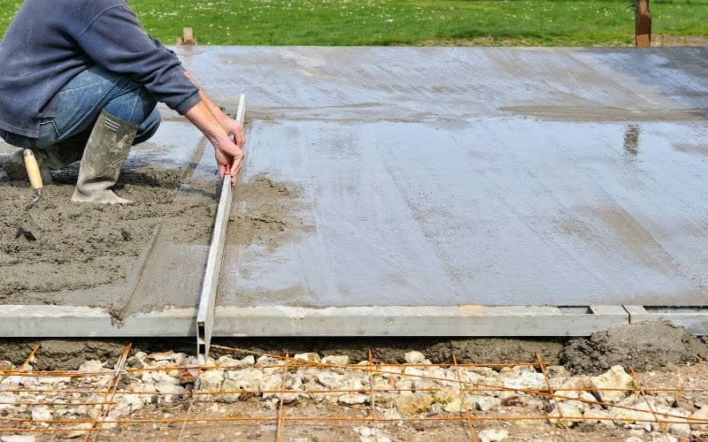 Worker screeding and edging a freshly poured concrete slab outdoors