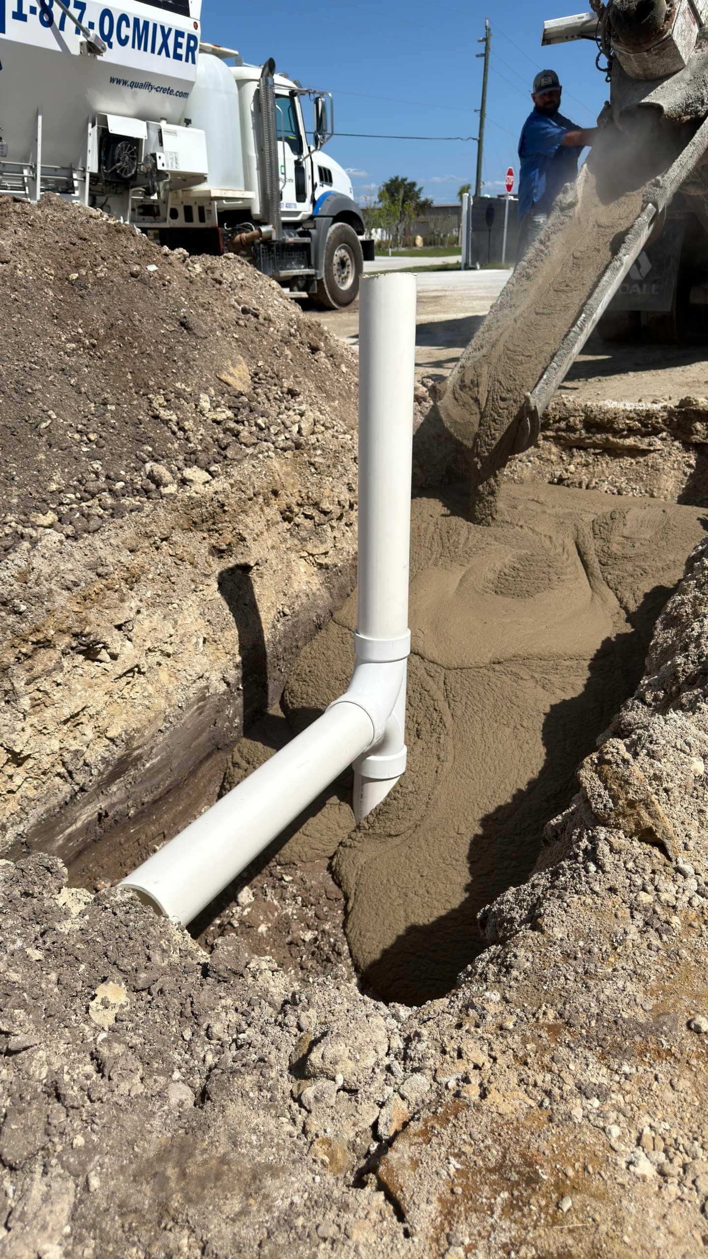 Quality-Crete mixer truck discharging fast setting flowable fill into a utility trench around a PVC pipe fitting