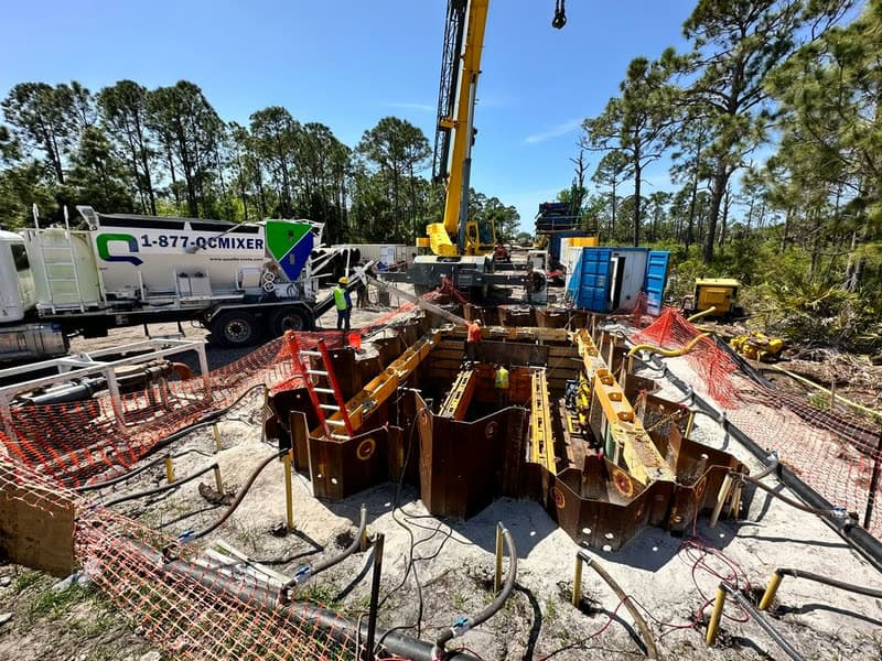 Deep shored excavation with steel trench boxes and a Quality-Crete mixer truck on site