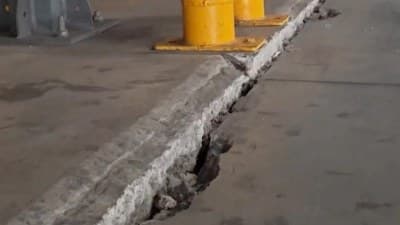 Cracked, settled concrete slab joint beside yellow bollards in a warehouse