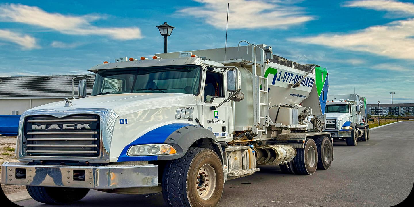 Two Quality-Crete volumetric mixer trucks parked on a paved road under a blue sky