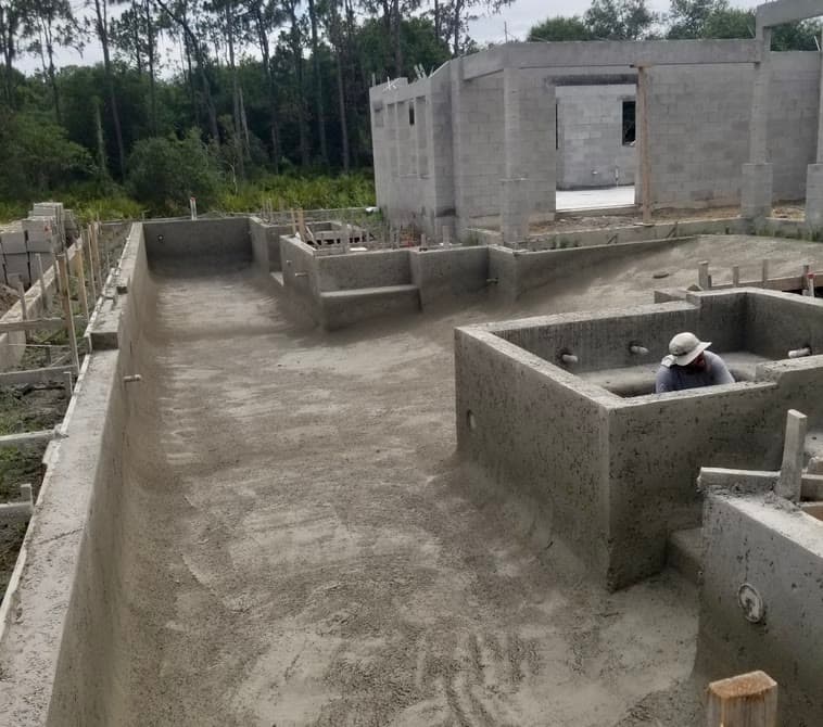 Shotcrete pool shell and retaining walls under construction beside a block building