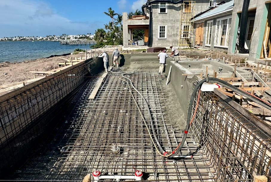 Crew shooting shotcrete over rebar for a pool shell beside a waterfront home