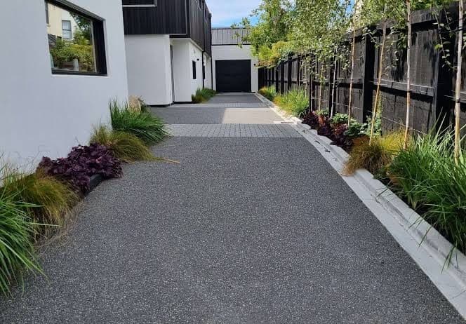 Concrete walkway between a house and landscaped fence line