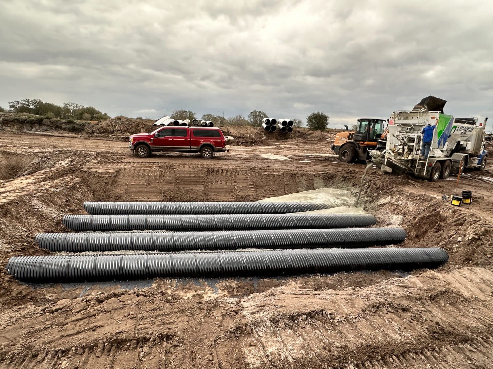 Culvert pipe staged on a rural site beside a Quality-Crete mixer